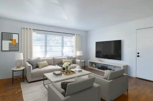 Bright living room with mid-century modern furniture, a wall-mounted TV, large window, and hardwood flooring.