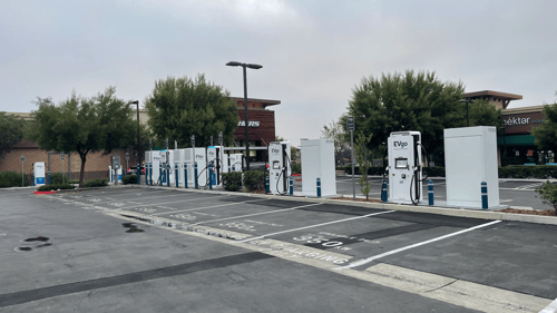 Several EVgo fast-charging units installed in marked parking spaces at a public charging station, with EVgo logos on the chargers, protective bollards around each unit