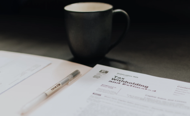 A tax form lies on a table beside a pen and a dark coffee mug, conveying a focused and work-oriented atmosphere.