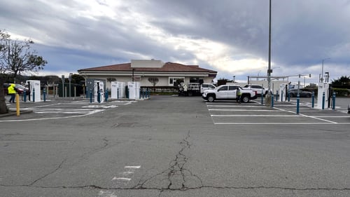 Several EVgo fast-charging units installed in marked parking spaces at a public charging station, with EVgo logos on the chargers, protective bollards around each unit