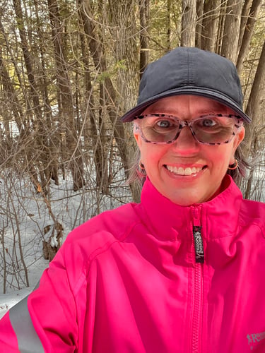 Selfie of Colleen wearing a pink jacket on a sunny day.