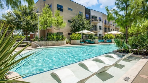 A swimming pool with sun loungers and a building in the background.