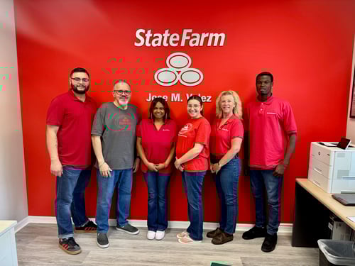 Agent Jose and his five team members all in red shirts and dark jeans standing together in front of a red wall with a State Farm logo.