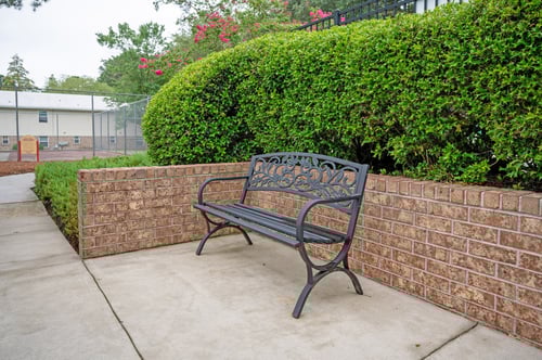 A black bench sits on a sidewalk next to a brick wall.