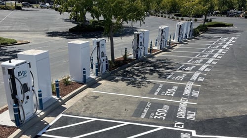 Several EVgo fast charging units installed in marked parking spaces at a public charging station, with EVgo logos on the chargers, protective bollards around each unit