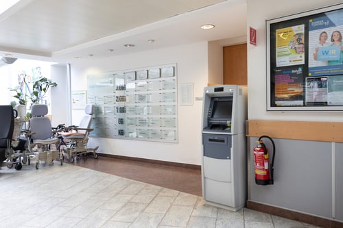 Schrägansicht des Bankomaten aus mittlerer Entfernung, die den gesamten Automaten und den umgebenden Bereich umfasst.