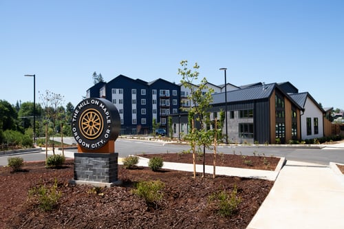 a building with a sign in front of it on a sidewalk at The Mill on Maple Apartments, Oregon, 97045