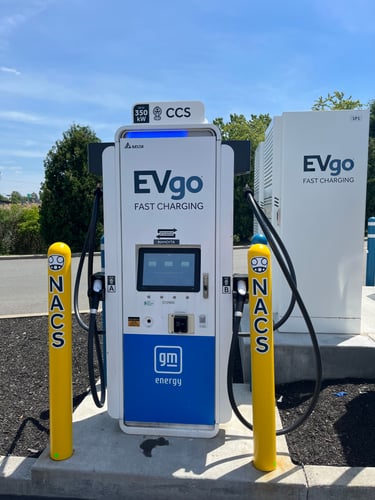NACS EVgo fast charging unit installed in marked parking space at a public charging station, with EVgo logos on the charger,  and yellow protective bollards around the unit