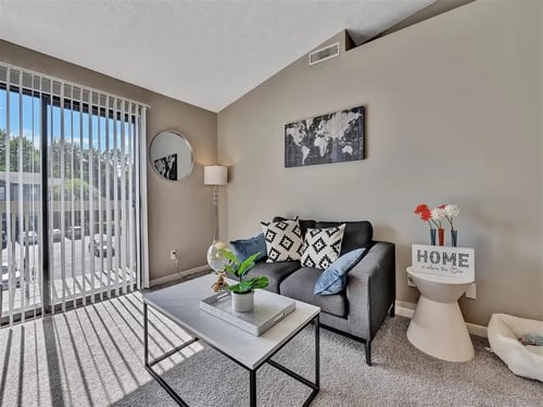 A living room with a grey couch, a coffee table, and a sign at The Reserve at Grand Valley Apartments, Milford 46150