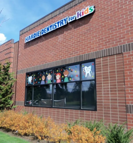 Exterior view of a red brick building featuring a "Hardie Dentistry for Kids" sign and a large window decorated with colorful tooth and children illustrations.