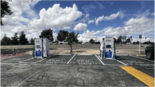 Several EVgo fast-charging units installed in marked parking spaces at a public charging station, with EVgo logos on the chargers, protective bollards around each unit