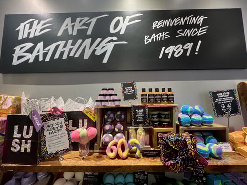 Display of packaged and unpackaged exclusive party products. Sign above reads The Art Of Bathing, Reinventing Baths Since 1989!