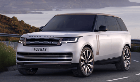 Front view of a silver Range Rover driving along a scenic coastal road.