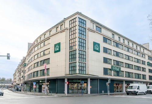 Façade extérieure moderne de l'hôtel B&B à l'angle d'une rue avec fenêtres vitrées et enseigne visible.