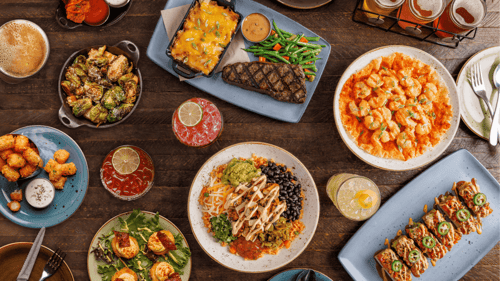 Large shareable feast with grilled steak, firecracker shrimp, brussels sprouts, a chicken bowl, tater tots, deviled eggs, and a beer flight.