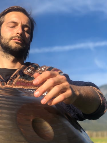 Der Handpan.World Vertreter aus Innsbruck sitzt im Grünen und spielt gefühlvoll eine Handpan. Seine Augen sind dabei geschlossen