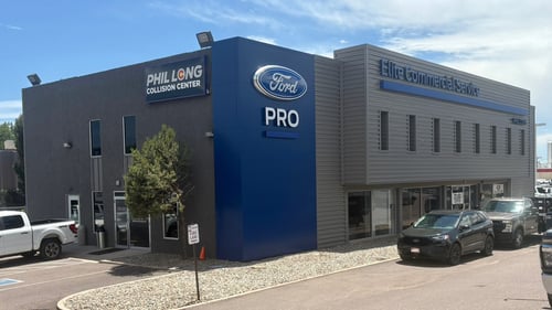 Exterior of Phil Long Collision Center and Ford Pro Elite Commercial Service building in Colorado Springs, Colorado, featuring modern gray and blue architecture, customer parking, and signage highlighting professional OEM-certified auto body repair and commercial vehicle services.