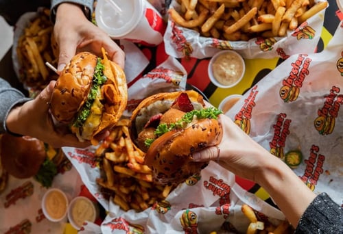 Close up of two people holding their burgers at Taystee's in Dearborn