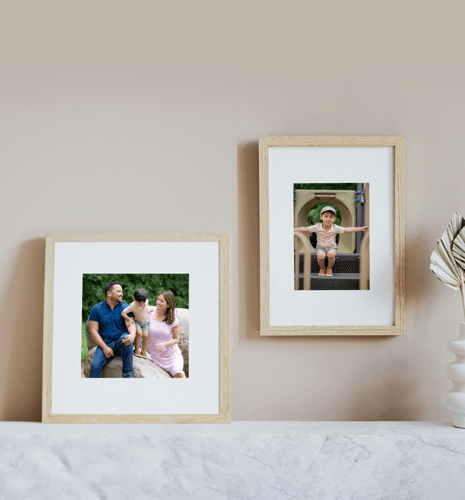 Two framed family photos on a light wall. Left shows smiling parents with child outdoors. Right shows a child in a play area, wearing a hat. Cozy atmosphere.