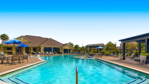 Swimming pool with chairs and umbrellas at the clubhouse at Grand Villas at Cinco Ranch, Katy, TX