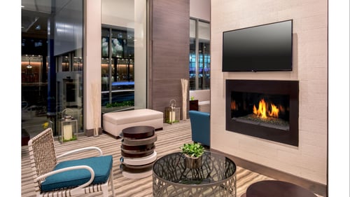 Lobby with seating area on left side facing an inset fireplace with a flatscreen TV above it.