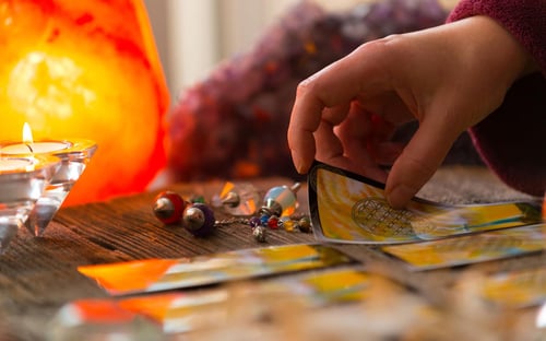 Psychic's hand doing a tarot card reading with a spread of yellow backed tarot cards and a glowing amber crystal near by.