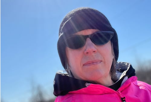 Selfie of Colleen in the outdoors, blue sky, with sun in background.