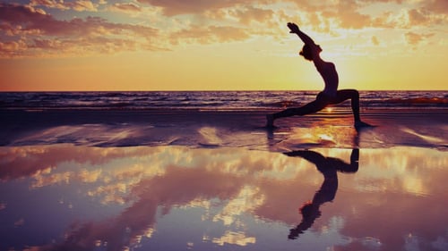 Person doing yoga on the beach during sunset
