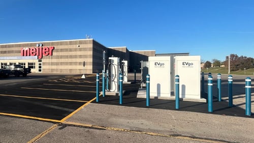 Several EVgo fast-charging units installed in marked parking spaces at a public charging station, with EVgo logos on the chargers, protective bollards around each unit