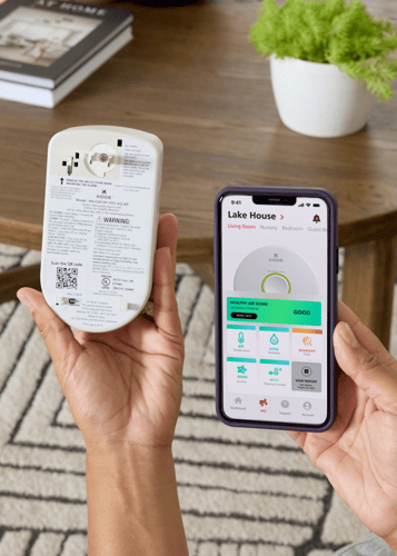 Le téléphone d'une personne affichant le rapport avancé sur la santé à domicile et tenant l'alarme intelligente de monoxyde de carbone avec surveillance de l'air intérieur.
