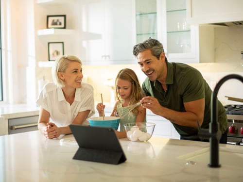 Family in kitchen cooking while watching a cooking video on laptop