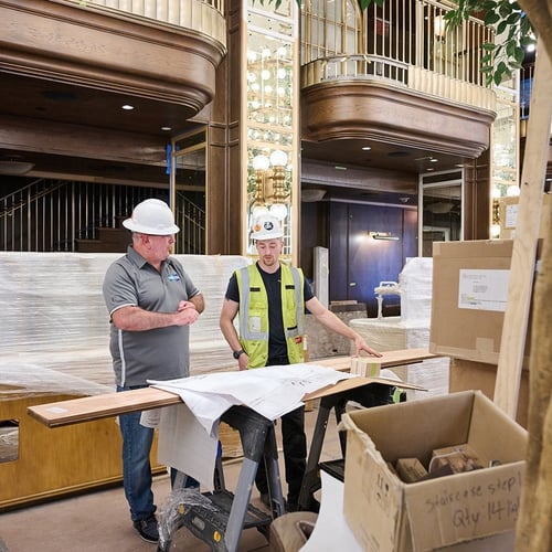 Two construction professionals in a partially completed interior reviewing blueprints on a job site