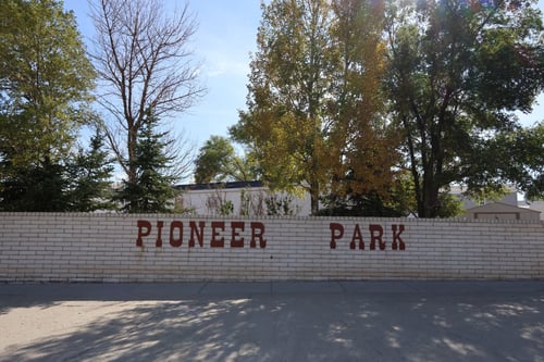The words "Pioneer Park" in western stylized letters that are dark red on a white brick wall