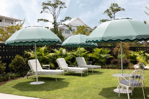 Outdoor seating area with green umbrellas and white chairs overlooking a lawn.