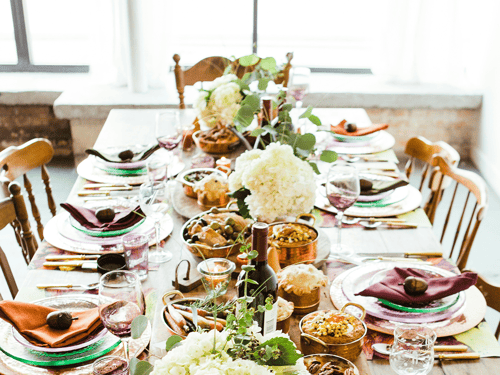 A beautifully set dining table adorned with vibrant plates, elegant glassware, and an array of dishes, complemented by flowers and greenery.