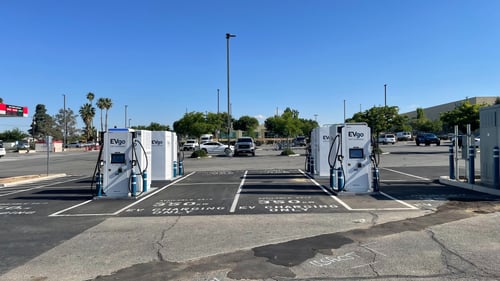 Several EVgo fast charging units installed in marked parking spaces at a public charging station, with EVgo logos on the chargers, protective bollards around each unit