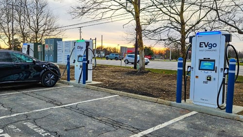 Several EVgo fast-charging units installed in marked parking spaces at a public charging station, with EVgo logos on the chargers, protective bollards around each unit