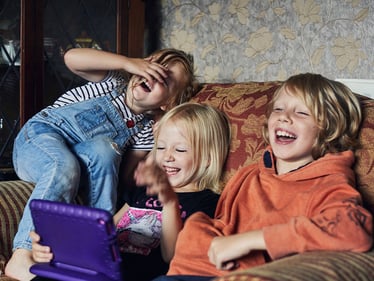 Kids laughing on a couch watching a tablet