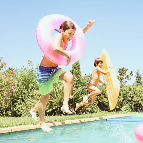 Children jumping into a swimming pool with colorful inflatable pool toys