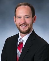 Dr. Joseph Benert smiling in front of a gray background.