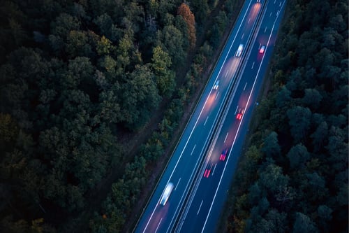 Highway through forest at night with vehicle light trails.