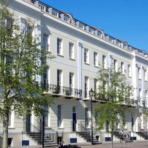 Knight Frank Cheltenham Estate Agents - A row of grand, white-stucco Regency terraced houses with iron balconies and sash windows in Cheltenham, UK.