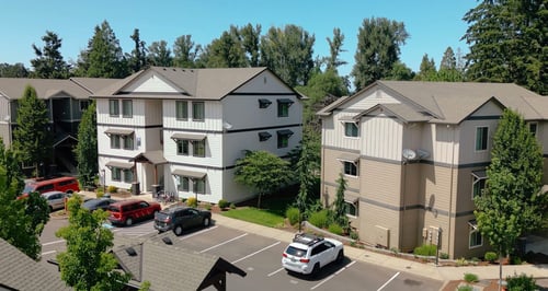A white and beige apartment complex with a parking lot in front at Silverplace Apartment Homes, Silverton, OR, 97381