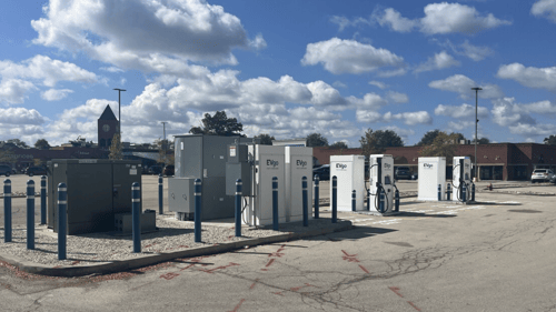 Several EVgo fast-charging units installed in marked parking spaces at a public charging station, with EVgo logos on the chargers, protective bollards around each unit