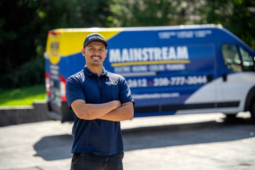 A Mainstream Electric, Heating, Cooling & Plumbing technician standing in front of the work truck smiling at the camera.