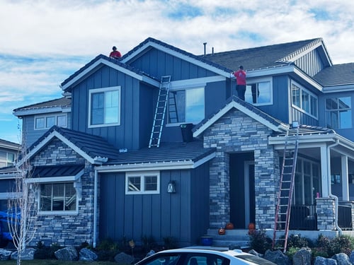 Two Preferred Lightscapes technicians in red shirts installing roofline lights from ladders on a two-storey home