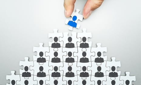 Pyramid made of up puzzle pieces with a blue silhouette representation of a person sitting on top of dark silhouettes.