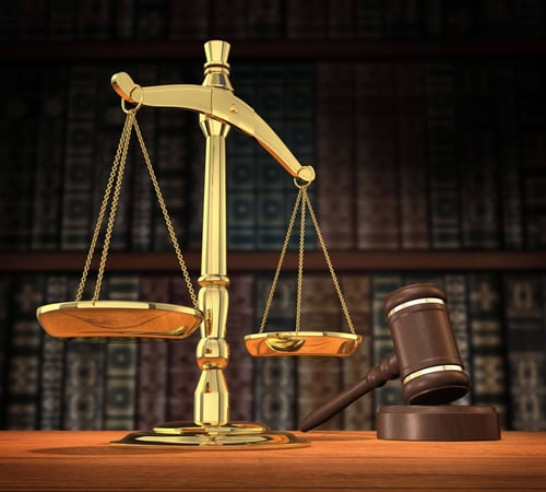 The scales of justice sitting next to a gavel on a brown desk.