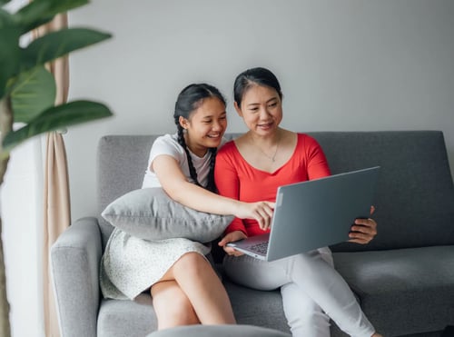 Mother and daughter sitting on a couch looking over a laptop.