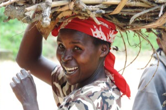 Smiling woman wearing red head scarf carrying baby on her back in colorful traditional fabric wrap at Rwandan community center